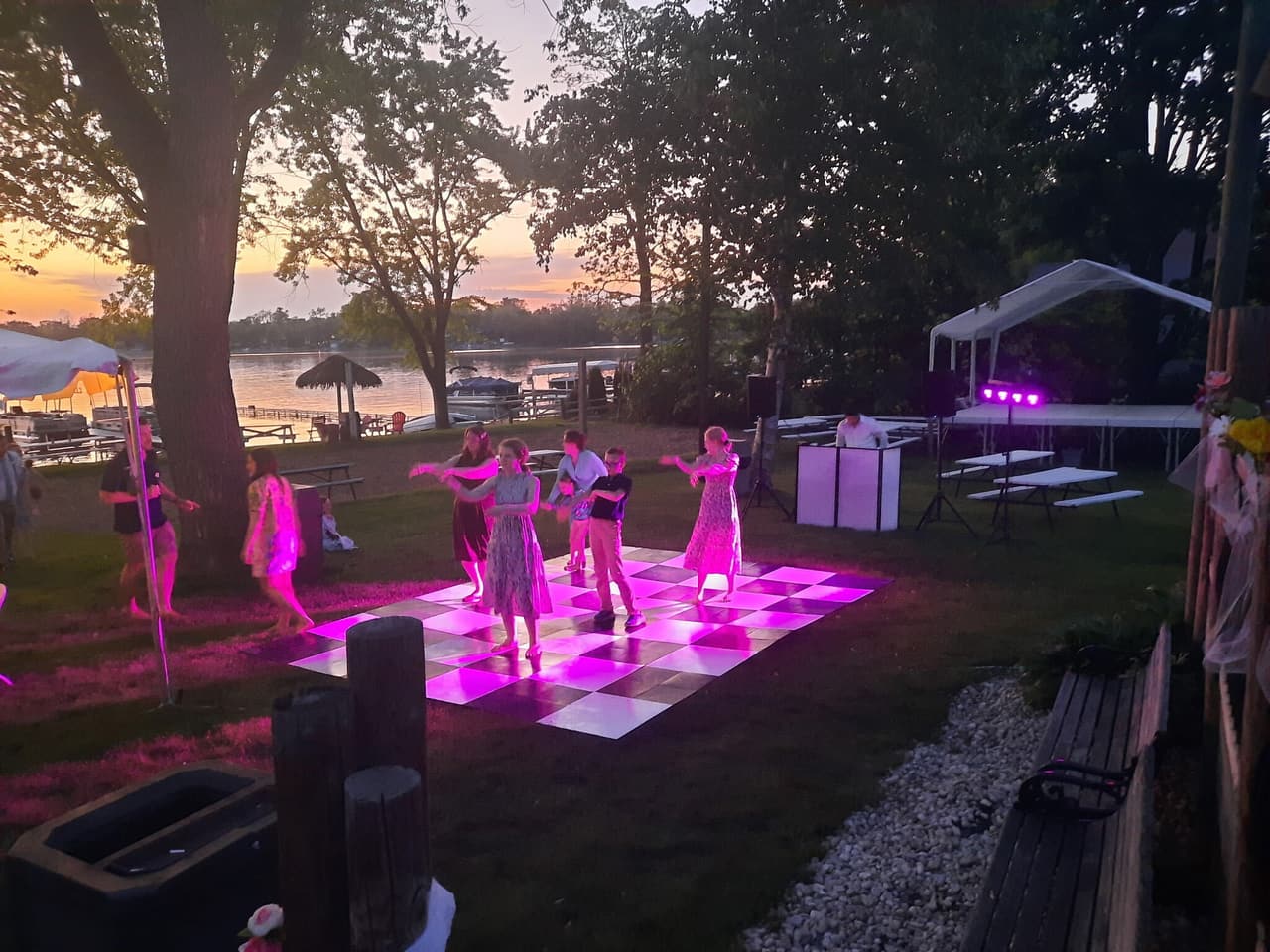 A lit-up dance floor on the lawn by the lake at dusk